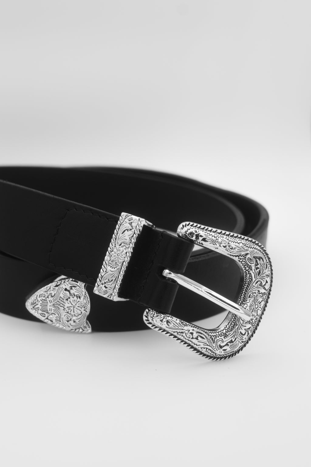 A black leather belt with an ornate silver-tone buckle, keeper, and tip, displayed on a light gray background.